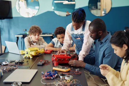 Téléchargez les photos : Portrait d'une adolescente noire construisant un robot avec un groupe diversifié d'enfants pendant les cours d'ingénierie à l'école - en image libre de droit