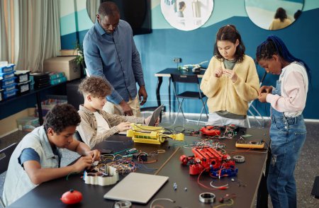 Photo for Diverse group of teenage children building robots together while enjoying engineering class in modern school - Royalty Free Image