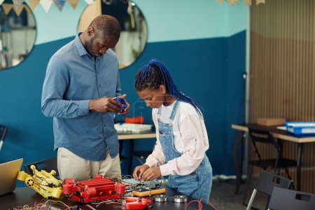 Foto de Retrato del profesor masculino ayudando a una joven afroamericana a construir un robot durante la clase de ingeniería en la escuela, espacio para copiar - Imagen libre de derechos