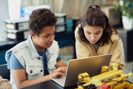 Téléchargez les photos : Portrait de garçon et de fille utilisant un ordinateur portable ensemble et programmant des robots pendant les cours d'ingénierie à l'école - en image libre de droit