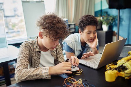 Foto de Retrato de dos chicos usando un portátil juntos y programando robots durante la clase de ingeniería en la escuela - Imagen libre de derechos
