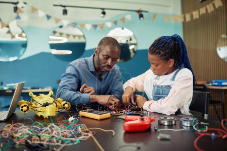 Téléchargez les photos : Portrait de jeune fille noire construisant des robots avec professeur masculin aidant pendant les cours d'ingénierie à l'école - en image libre de droit