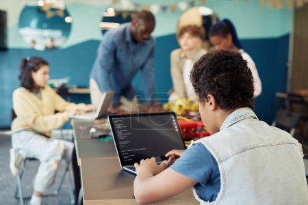 Téléchargez les photos : Vue arrière d'un garçon utilisant un ordinateur portable dans une classe d'ingénierie et des robots de programmation, espace de copie - en image libre de droit