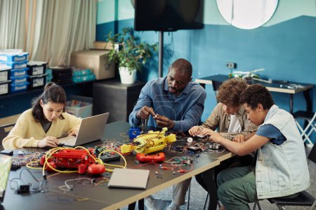 Photo for Portrait of black male teacher building robots with diverse group of children in engineering class at modern school, copy space - Royalty Free Image