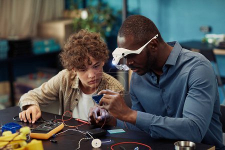 Photo for Portrait of young teenage boy building robots in engineering class with male teacher helping - Royalty Free Image
