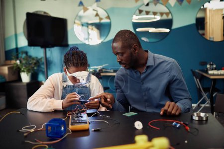 Téléchargez les photos : Portrait de robot de construction de jeune fille noire en classe d'ingénierie avec professeur masculin aidant - en image libre de droit