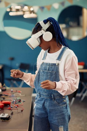 Photo for Vertical portrait of black teenage girl using VR technology in engineering class and looking around - Royalty Free Image