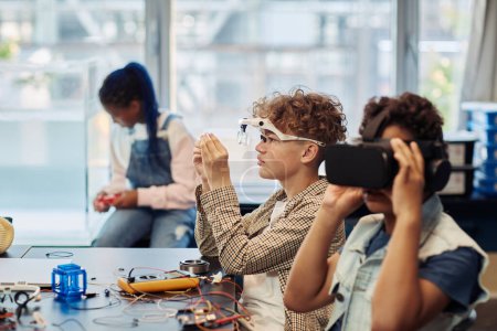 Photo for Side view portrait of two kids building robots in engineering class and using VR technology - Royalty Free Image