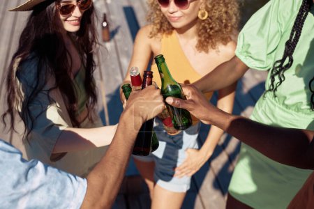 Photo for High angle view of young people clinking bottles while enjoying Summer vacation in sunlight - Royalty Free Image