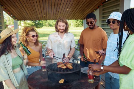 Photo for Diverse group of young people grilling meat during barbeque party outdoors in Summer and drinking beer - Royalty Free Image