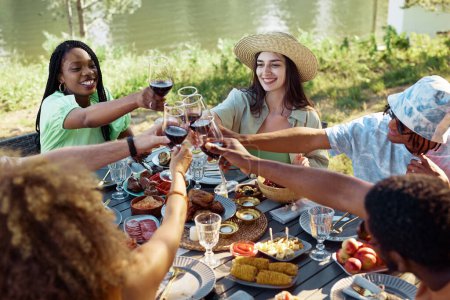 Foto de Alto ángulo diverso grupo de jóvenes brindando con copas de vino durante la cena al aire libre en verano - Imagen libre de derechos