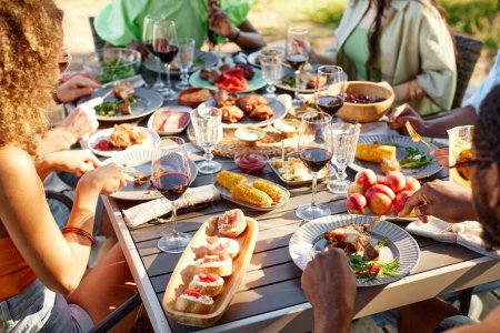 Téléchargez les photos : Table à manger rustique à l'extérieur avec délicieux festin fait maison et les gens qui apprécient le repas d'été ensemble, copier l'espace - en image libre de droit