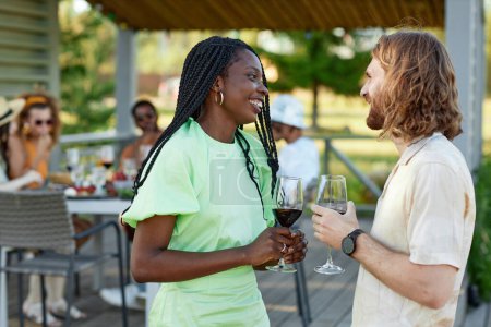 Téléchargez les photos : Portrait de jeune couple bavardant et dégustant un verre de vin lors d'une fête en plein air avec des amis en été, espace de copie - en image libre de droit