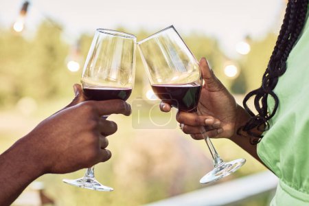 Photo for Close up of black young couple toasting and enjoying glass of wine at terrace during romantic date outdoors in Summer - Royalty Free Image