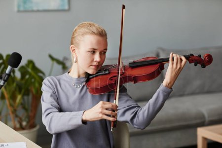 Photo for Portrait of blonde young woman playing violin at home or practicing in music studio, copy space - Royalty Free Image