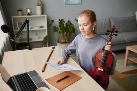 Téléchargez les photos : Portrait en grand angle d'une femme blonde jouant du violon à la maison et regardant des feuilles de musique tout en composant, copiant de l'espace - en image libre de droit