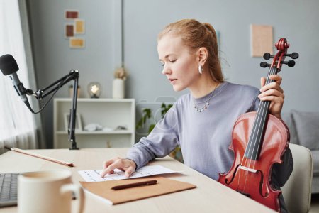 Téléchargez les photos : Portrait latéral de femme blonde jouant du violon à la maison et regardant des feuilles de musique tout en composant, copier l'espace - en image libre de droit
