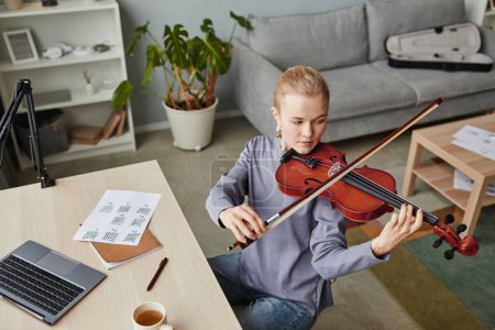 Foto de Retrato en ángulo alto de una joven rubia tocando el violín en casa o practicando en un estudio de música, espacio para copiar - Imagen libre de derechos