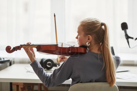 Foto de Vista trasera de la joven rubia tocando el violín en el estudio contra la luz de la ventana, espacio para copiar - Imagen libre de derechos