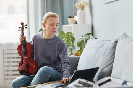 Photo for Portrait of blonde young woman playing violin at home and watching online lesson, copy space - Royalty Free Image