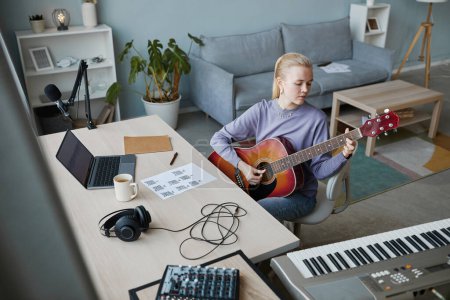 Téléchargez les photos : Portrait en grand angle d'une jeune femme blonde jouant de la guitare à la maison et composant de la musique, espace de copie - en image libre de droit