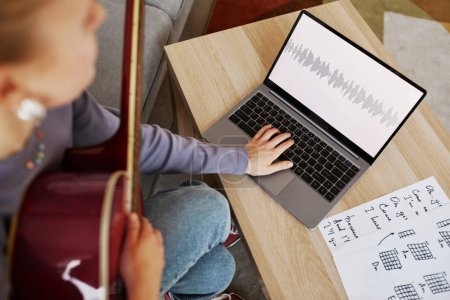 Téléchargez les photos : Grand angle gros plan de jeune femme jouant de la guitare à la maison et composant de la musique via un ordinateur portable, espace de copie - en image libre de droit