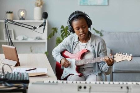 Foto de Retrato de una joven mujer negra tocando la guitarra eléctrica y grabando canciones en el estudio en casa, espacio para copiar - Imagen libre de derechos
