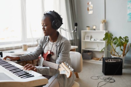 Téléchargez les photos : Portrait minimal de jeune femme noire jouant du synthétiseur et composant de la musique à la maison, espace de copie - en image libre de droit