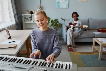 Foto de Retrato de una joven rubia tocando sintetizador en casa y componiendo música, espacio para copiar - Imagen libre de derechos