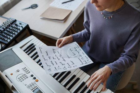 Foto de Alto ángulo de primer plano de joven músico tocando sintetizador en casa y sosteniendo la letra de la canción hoja, espacio de copia - Imagen libre de derechos
