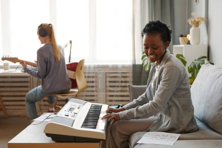 Téléchargez les photos : Portrait latéral d'une femme noire souriante jouant du synthétiseur à la maison et composant de la musique en studio, espace de copie - en image libre de droit