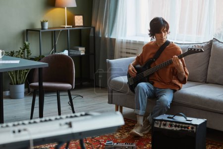 Téléchargez les photos : Portrait complet de jeune homme jouant de la guitare électrique dans un confortable studio de musique maison, espace de copie - en image libre de droit