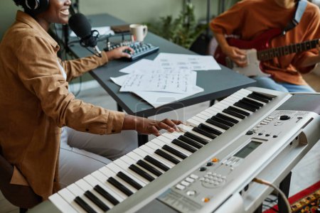 Téléchargez les photos : Gros plan de jeune femme noire pressant des touches de piano tout en composant de la musique avec un groupe de jeunes musiciens - en image libre de droit