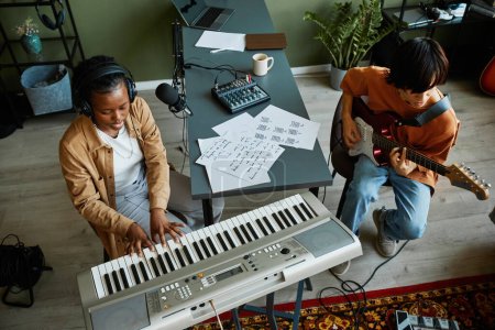 Téléchargez les photos : Vue de dessus à deux jeunes musiciens jouant des instruments ensemble dans le confortable home studio - en image libre de droit