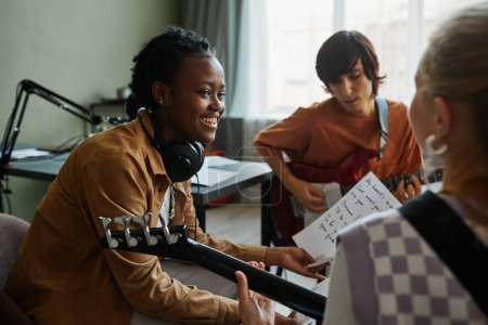 Photo for Side view portrait of black young woman writing music with band and smiling happily - Royalty Free Image