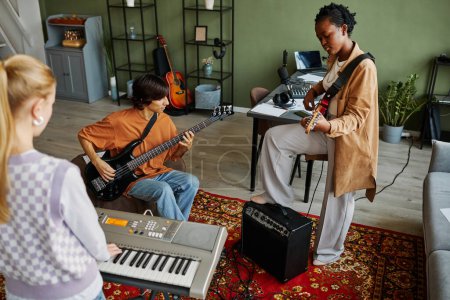 Téléchargez les photos : Plan dynamique d'un jeune groupe de musique jouant des instruments ensemble tout en pratiquant dans un studio confortable - en image libre de droit