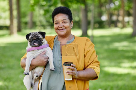 Téléchargez les photos : Portrait taille haute de femme noire mature tenant chien chiot mignon à l'extérieur et souriant à la caméra tout en appréciant la promenade dans le parc ensemble - en image libre de droit