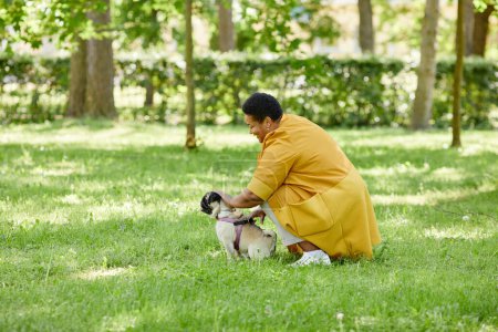 Photo for Side view portrait of mature black woman training cute dog in green park and smiling, copy space - Royalty Free Image
