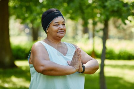 Téléchargez les photos : Portrait taille haute de femme noire mature faisant du yoga à l'extérieur dans un parc verdoyant et regardant loin avec attention, copiez l'espace - en image libre de droit