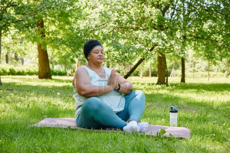 Téléchargez les photos : Portrait complet de femme noire en surpoids faisant du yoga à l'extérieur et méditant avec les yeux fermés dans le parc, espace de copie - en image libre de droit