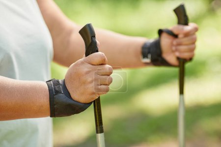Photo for Close up of overweight woman walking outdoors with nordic poles and enjoying cardio workout, copy space - Royalty Free Image
