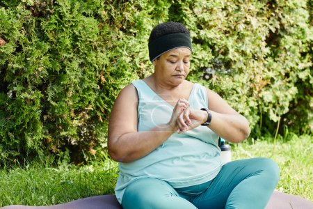 Téléchargez les photos : Portrait de femme noire mature regardant smartwatch tout en prenant une pause dans l'entraînement en plein air - en image libre de droit