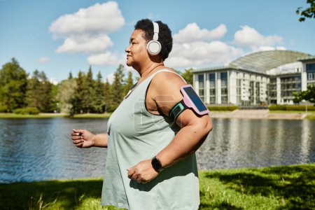Téléchargez les photos : Vue latérale portrait de femme noire mature courant à l'extérieur et portant des écouteurs profitant de l'entraînement - en image libre de droit