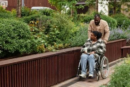 Photo for Full length portrait of black adult couple with partner in wheelchair enjoying walk together in city garden, copy space - Royalty Free Image