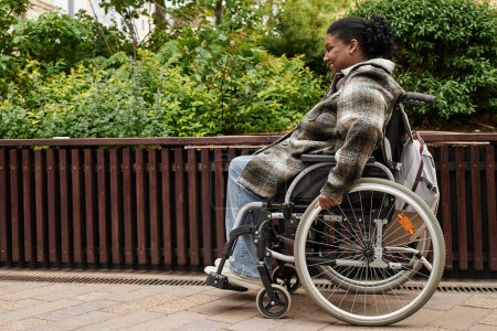Téléchargez les photos : Portrait latéral de femme noire souriante avec handicap dans le jardin de la ville d'automne, espace de copie - en image libre de droit