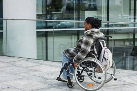 Téléchargez les photos : Prise de vue complète d'une femme noire adulte en fauteuil roulant se déplaçant en ville, espace de copie - en image libre de droit