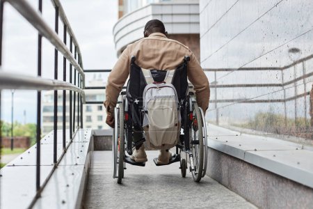 Téléchargez les photos : Vue arrière de l'homme handicapé poussant la roue en fauteuil roulant tout en descendant la rampe dans la ville, espace de copie - en image libre de droit