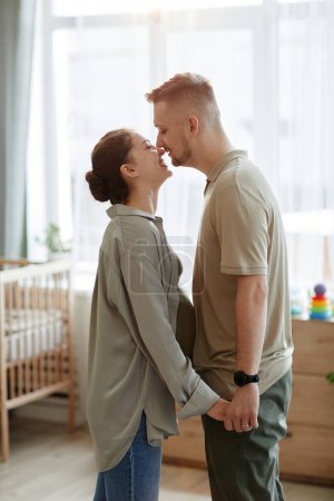 Photo for Happy young couple kissing in kid room in expectation of their baby - Royalty Free Image