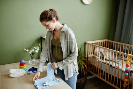 Foto de Mujer embarazada joven preparando cosas para su bebé de pie en la habitación del niño - Imagen libre de derechos