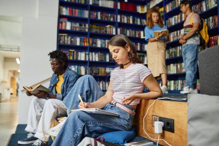 Foto de Vibrante retrato de la vista lateral de la mujer joven haciendo la tarea en la biblioteca de la universidad con los estudiantes en el fondo, espacio de copia - Imagen libre de derechos